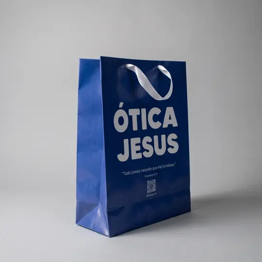 Sacola de papel azul com a logo grande em branco e alça de fita branca
