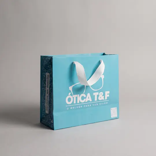 Sacola de papel azul-clara, mais larga, com estampa na lateral e alça de fita branca
